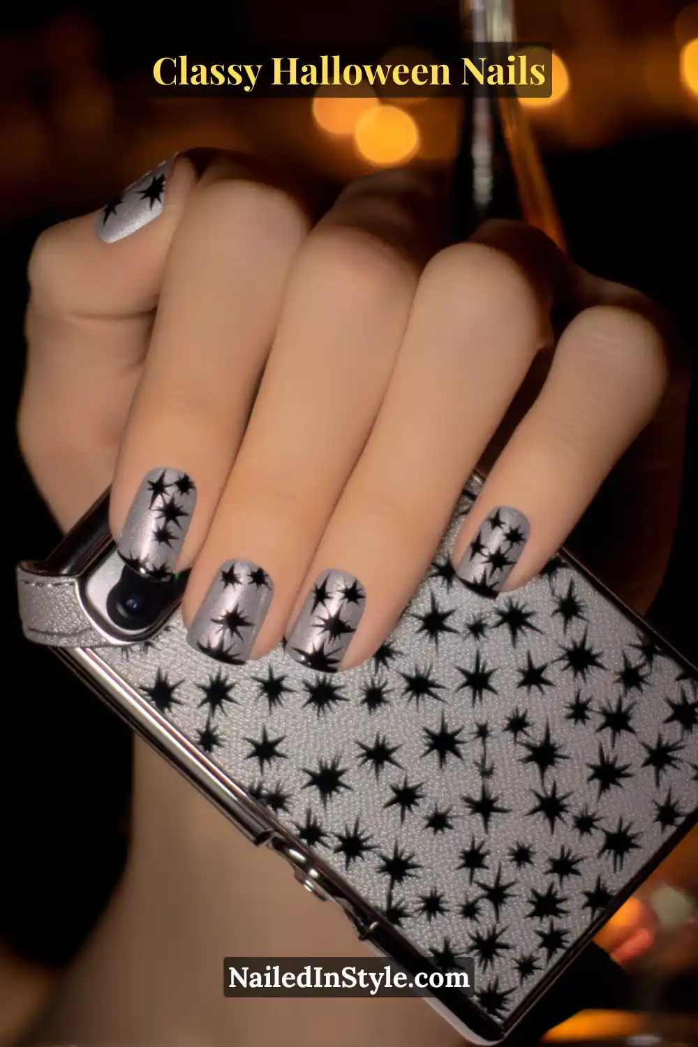 Short square nails brushed in sterling silver with glossy black star pin-dot accents near the base, creating a 3D jewel-like shimmer that sparkles under soft Halloween light.