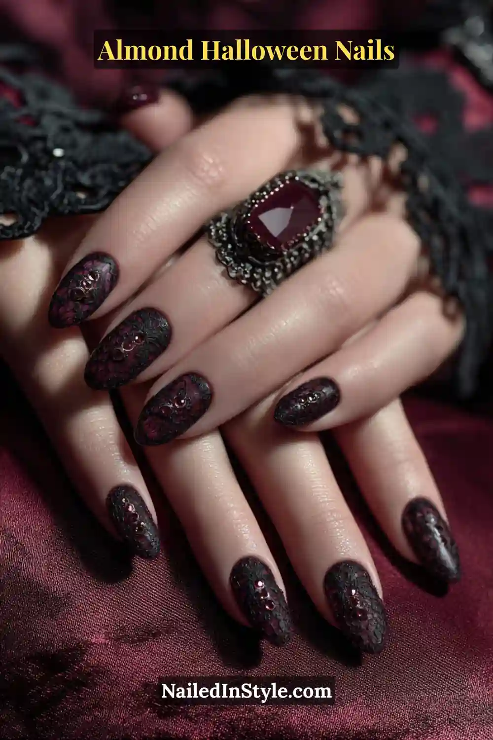 Close-up almond nails with embossed black lace texture and tiny garnet crystal drops near the cuticle, glossy finish with deep red undertones, Almond Halloween Nails.
