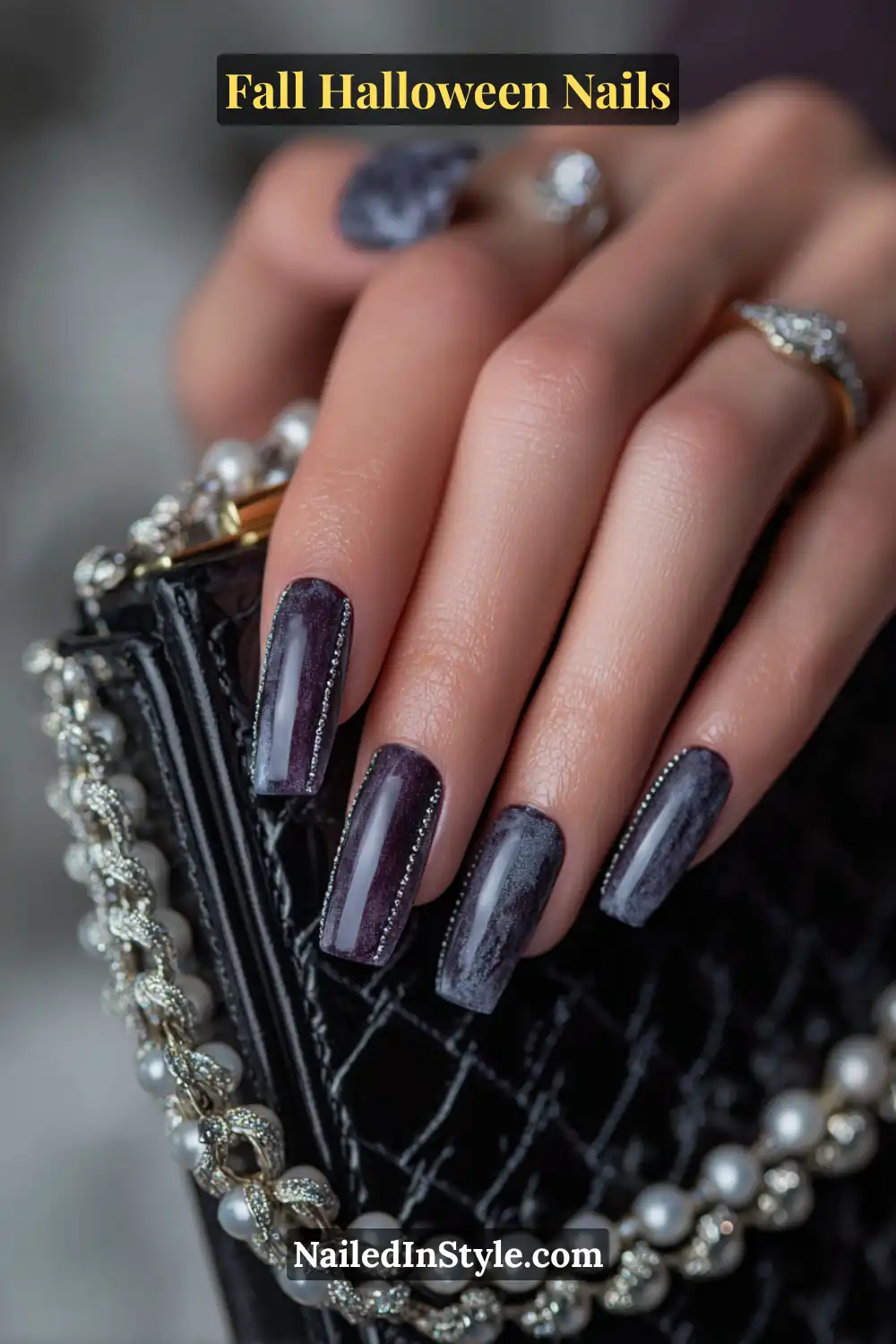 Medium square nails in deep midnight violet with a soft velvet finish and razor-thin pearl linework, styled alongside a black quilted clutch and delicate jewelry for a moody, luxe vibe.