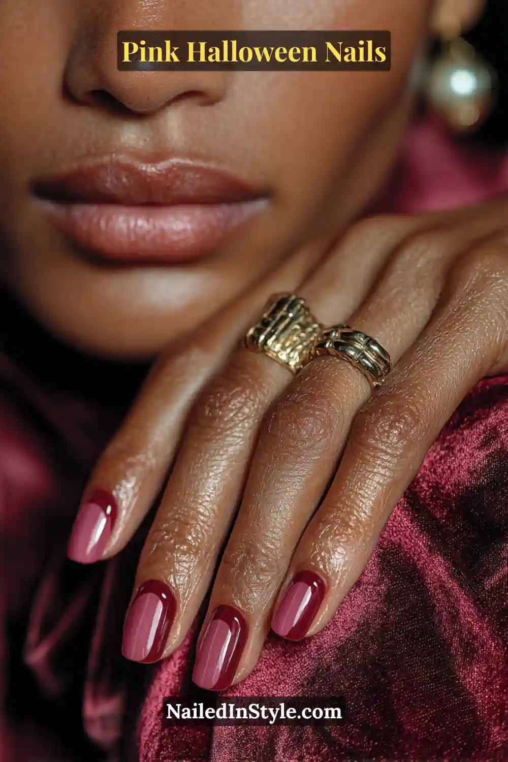 Pink Halloween nails featuring a velvet raspberry base with glossy oxblood half-moon cuticles on medium coffin nails, styled with gold statement rings and rich textures.