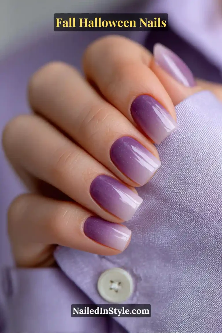 Short squoval nails in a smoky violet-to-ash ombré with a satin-gloss finish, styled against a lilac blouse for a polished autumn-Halloween transition look.