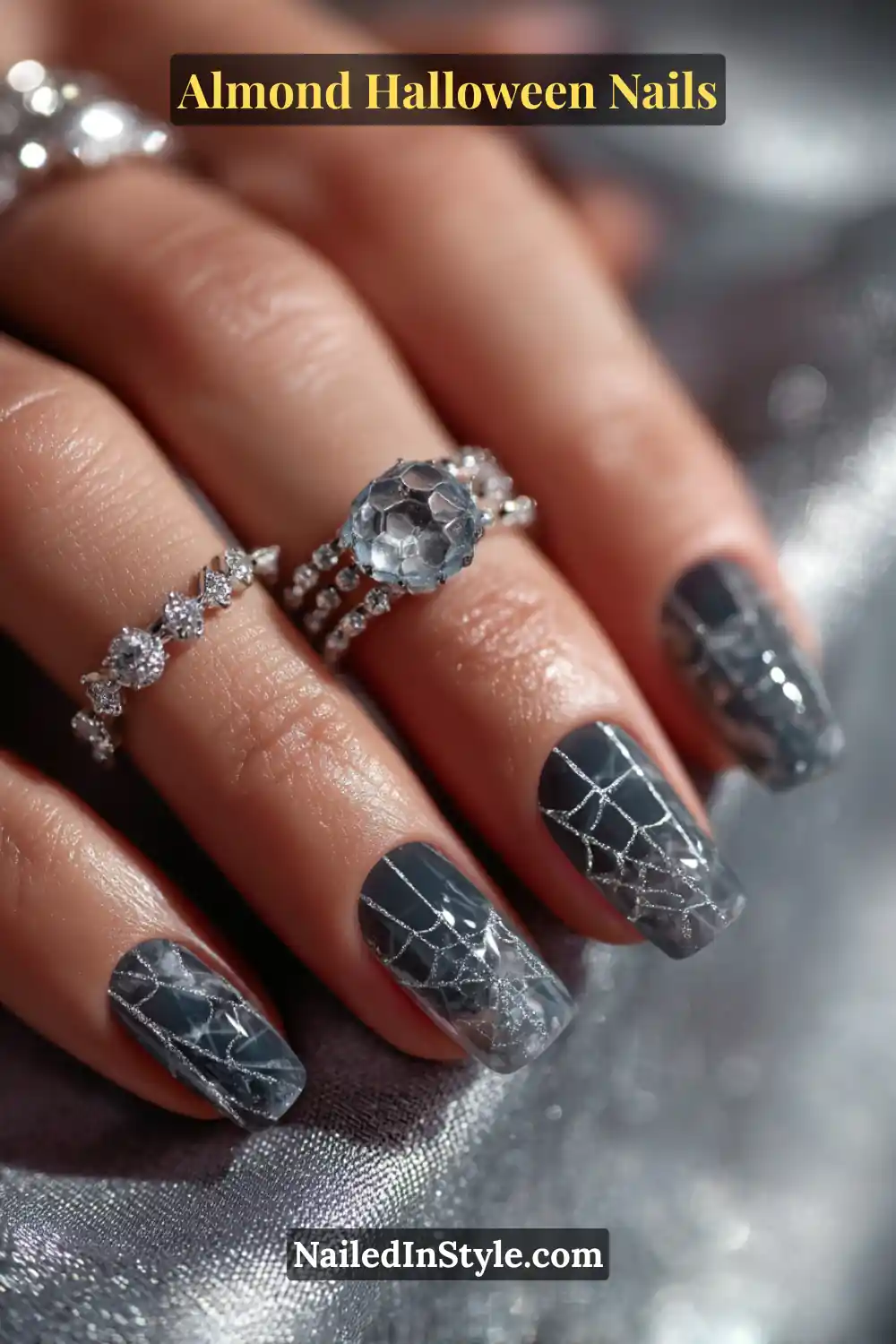 Close-up almond nails in sheer graphite with fine silver web patterns and crystal gem encapsulated mid-nail, glossy finish catching metallic light, Almond Halloween Nails.