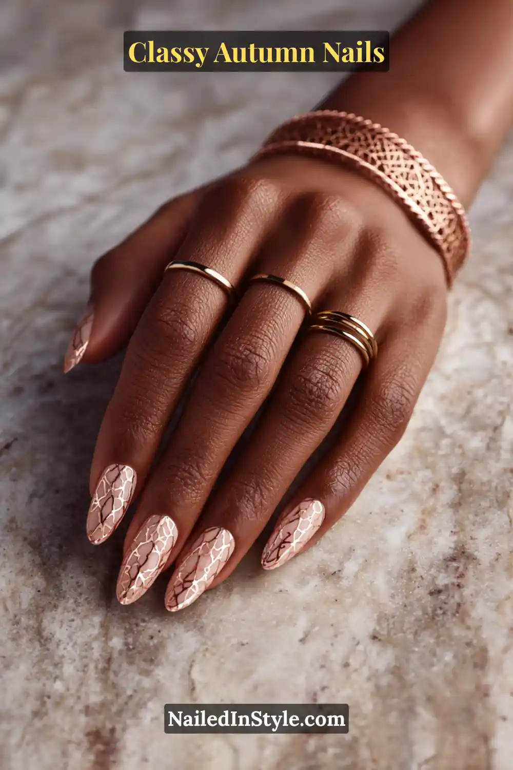 Almond autumn nails with sheer camel base and delicate copper lattice accents, styled with gold rings.