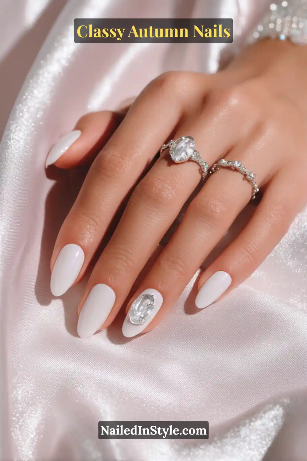 Almond nails in porcelain white with a single pewter cameo charm accent, styled with silver gemstone rings.