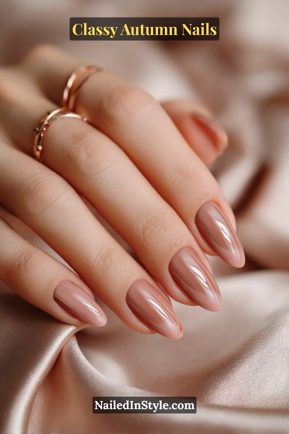 Almond autumn nails in soft beige with glossy rosewood droplet accents near the lunula, paired with rose-gold rings.