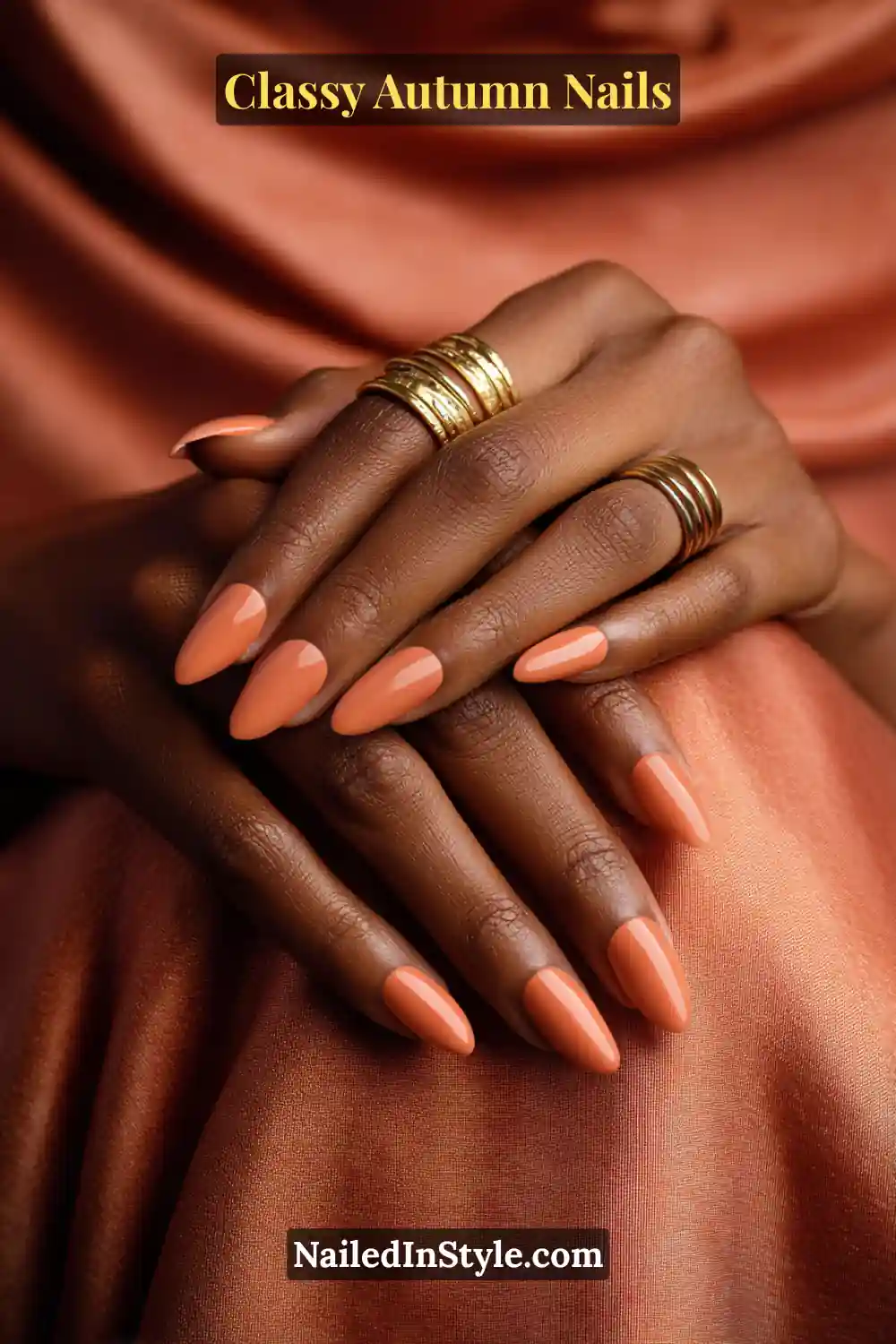 Classy Autumn Nails Almond autumn nails in muted terracotta with a silk-sheen finish, styled with gold rings on warm satin fabric.