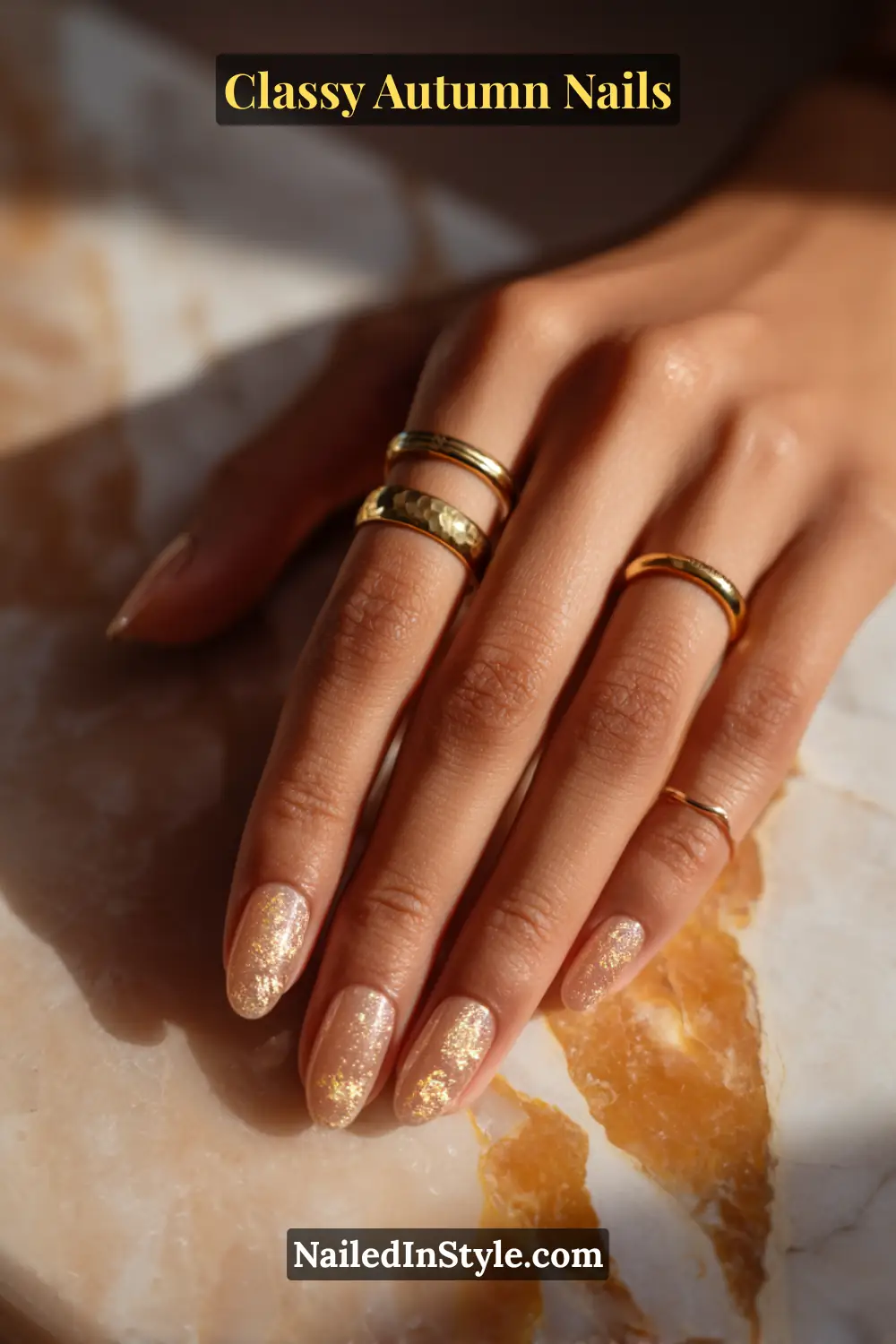 Almond nails with translucent amber polish featuring a subtle gold micro-crackle effect on the top third, paired with gold rings in warm sunlight.
