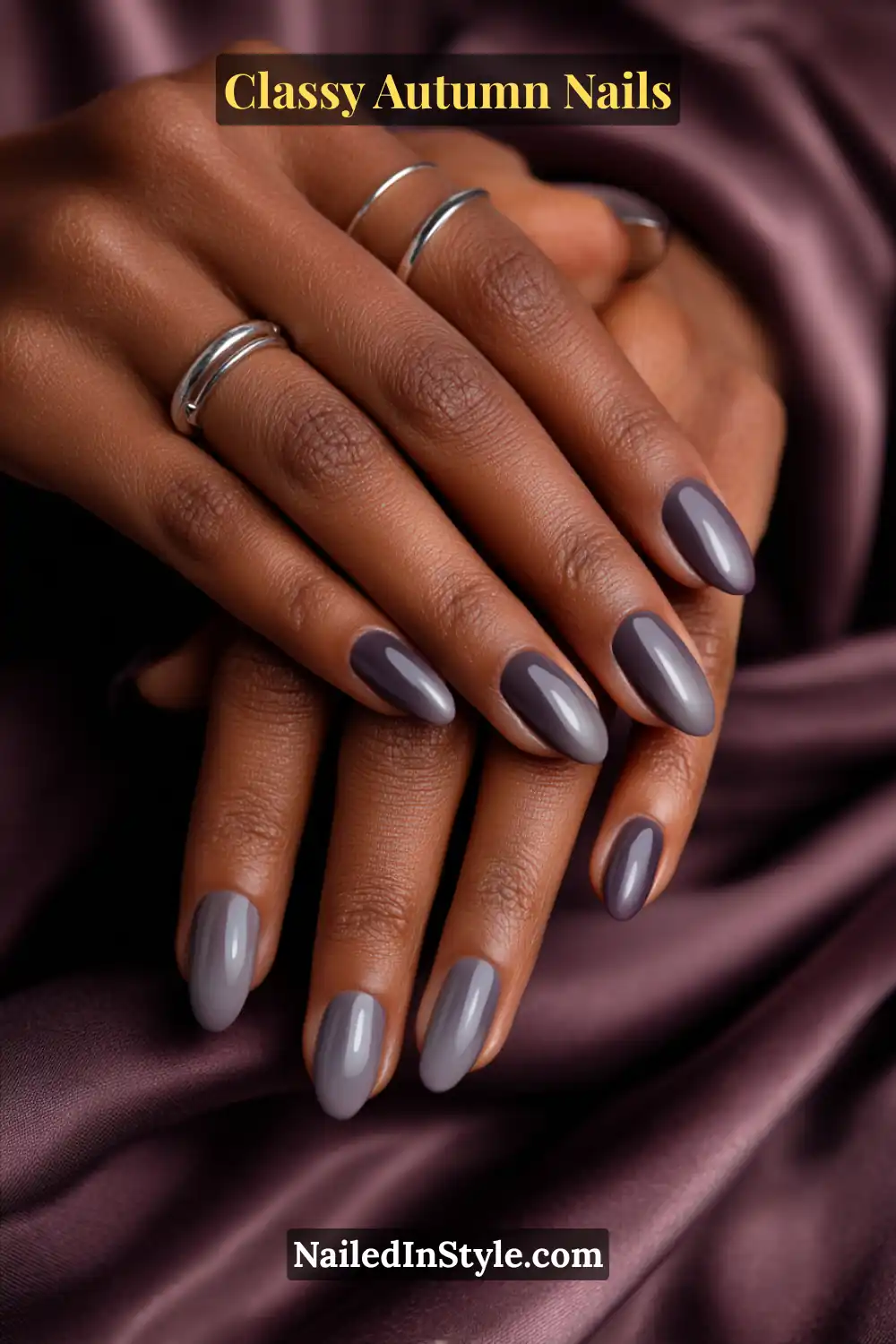 Oval nails featuring a chic gradient from smoky gray to deep raisin purple, styled against satin fabric with silver rings.
