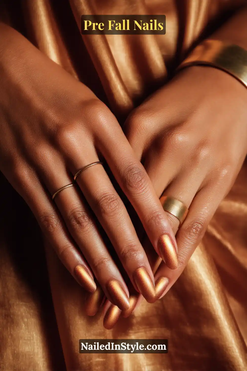 Almond nails with soft bronze aura glow centered above the lunula, styled on deep skin with gold jewelry and bronze satin fabric.