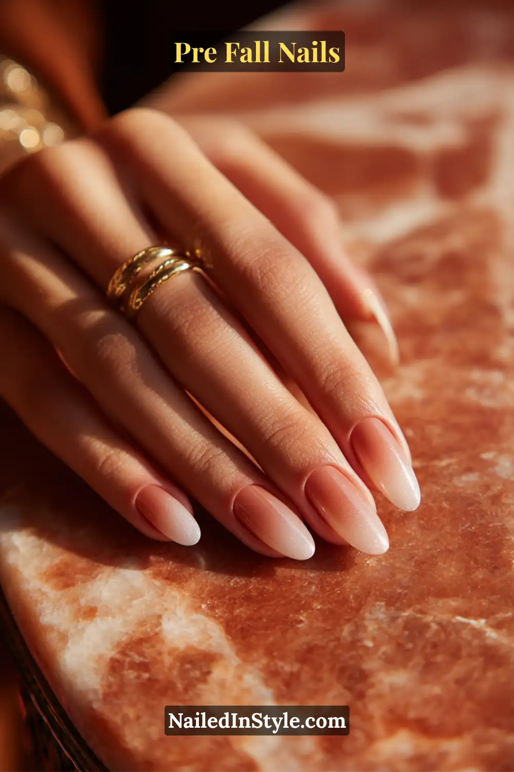 Almond nails featuring a ginger-spice fade blending softly into clear glossy tips, styled with gold rings on a warm marble surface.