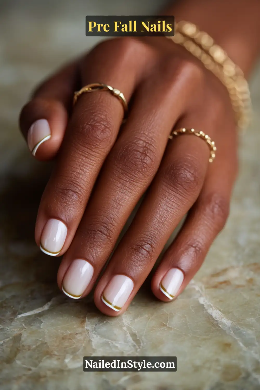 Short square nails with sheer nude bases and thin muted olive tips, paired with delicate gold rings on deep skin tone.
