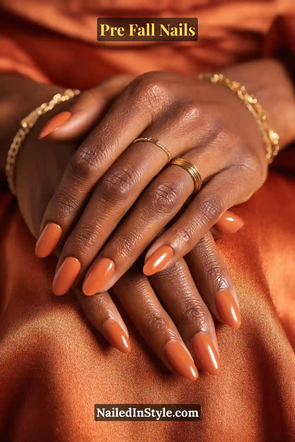 Oval nails coated in a translucent pumpkin-spice jelly gloss, styled with gold rings and burnt orange satin fabric background.