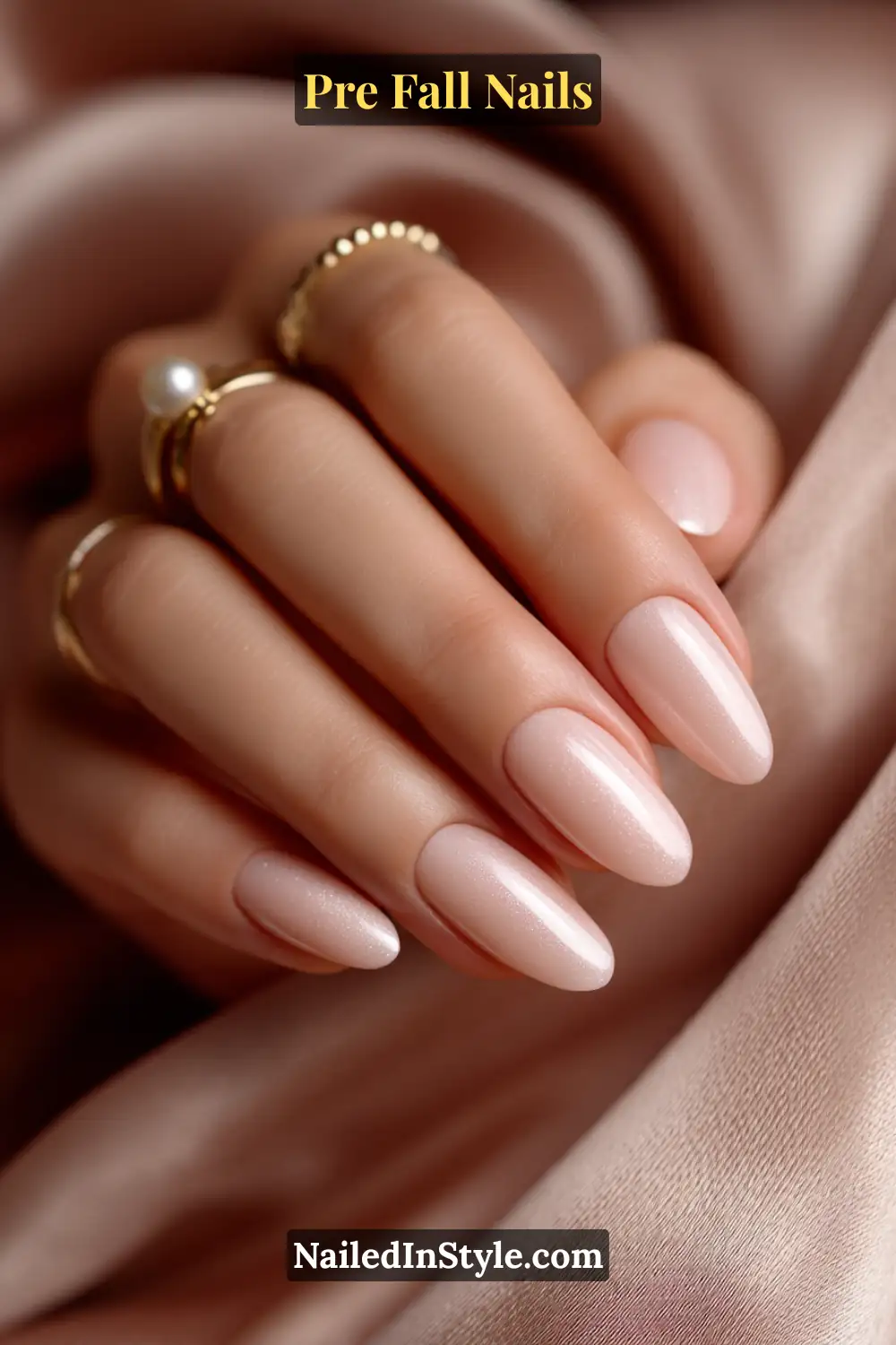 Pre Fall Nails Almond nails in soft sepia nude with a smooth satin cashmere finish, styled with gold and pearl rings on blush silk fabric.