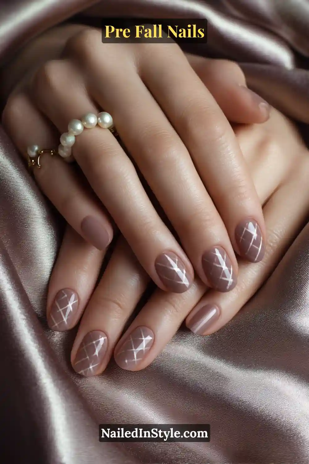 Squoval nails with a sheer nude base and fine taupe crisscross lines resembling a soft tweed pattern, styled with pearl rings on satin fabric.