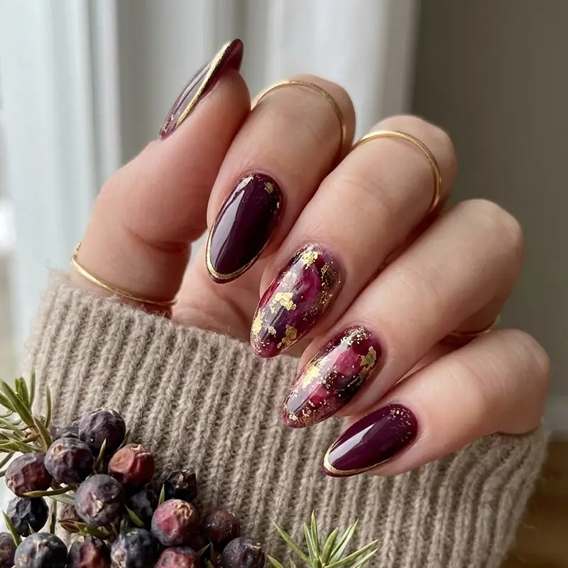 Dark berry plum almond nails decorated with gold leaf flakes and a delicate gold rim around the cuticle for February nail ideas.