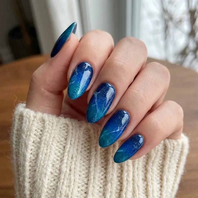 A hand displaying glossy almond-shaped nails with a mesmerizing nautical blue marble design and fine shimmer for February nail ideas.
