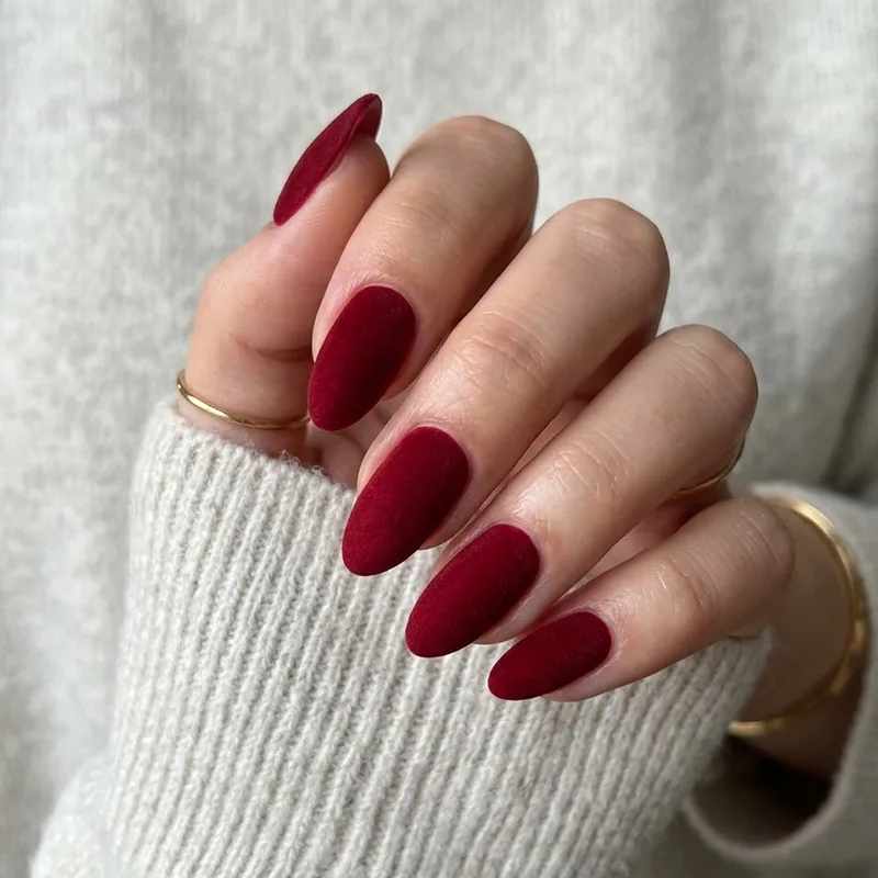 A hand wearing deep red almond-shaped nails with a soft, textured matte velvet finish for February nail ideas.