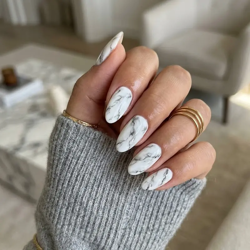 A hand wearing elegant white and grey marble patterned almond nails for February nail ideas.