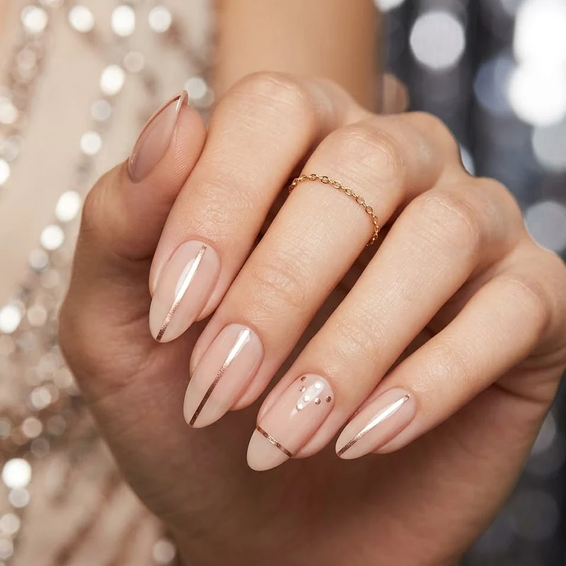 Prom Nails: Your Ultimate Guide to Stunning Styles and Techniques 2026 9 Professional close-up of almond-shaped prom nails featuring a glossy nude base with thin rose gold metallic vertical stripes and delicate dot accents against a sparkling bokeh background.