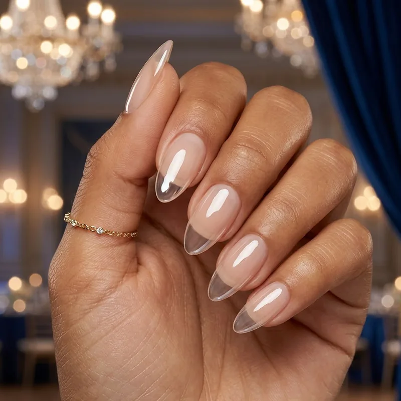 Prom Nails: Your Ultimate Guide to Stunning Styles and Techniques 2026 11 A professional close-up of elegant almond-shaped prom nails featuring a crystal-clear glass shine gel finish with a soft nude base against a blurred ballroom background with chandeliers.