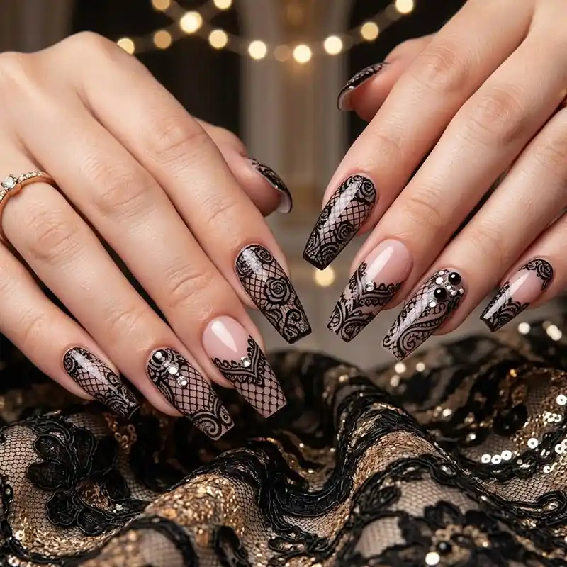 Prom Nails: Your Ultimate Guide to Stunning Styles and Techniques 2026 15 A close-up of long coffin-shaped prom nails featuring intricate black lace patterns, deep V-French tips, and rhinestone embellishments on a nude base, resting against black and gold sequined fabric.