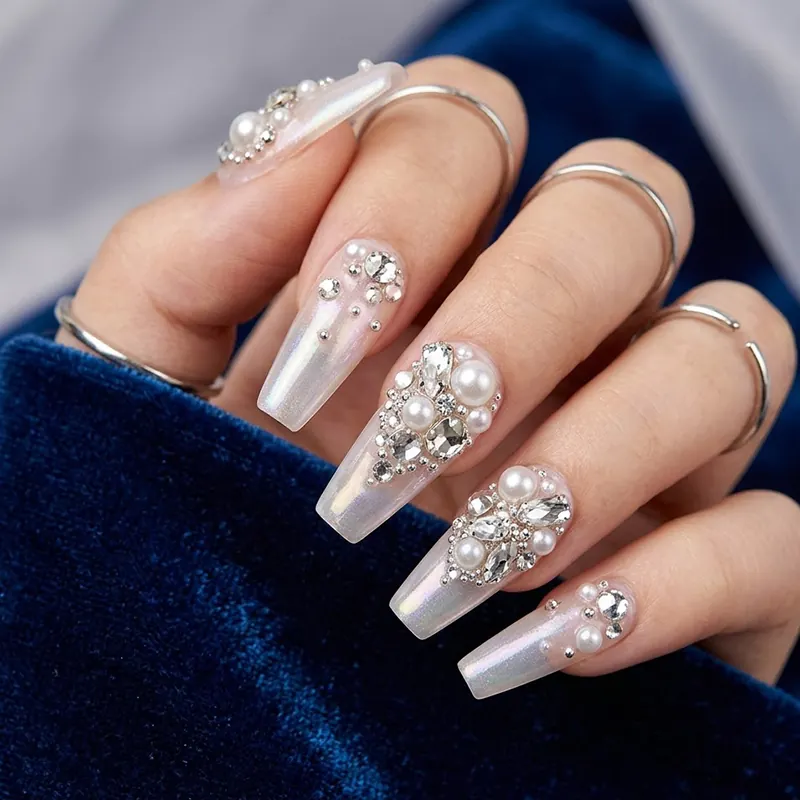 Prom Nails: Your Ultimate Guide to Stunning Styles and Techniques 2026 6 A close-up of long, iridescent coffin-shaped prom nails featuring intricate 3D embellishments of white pearls and sparkling gemstones against a textured blue velvet background.