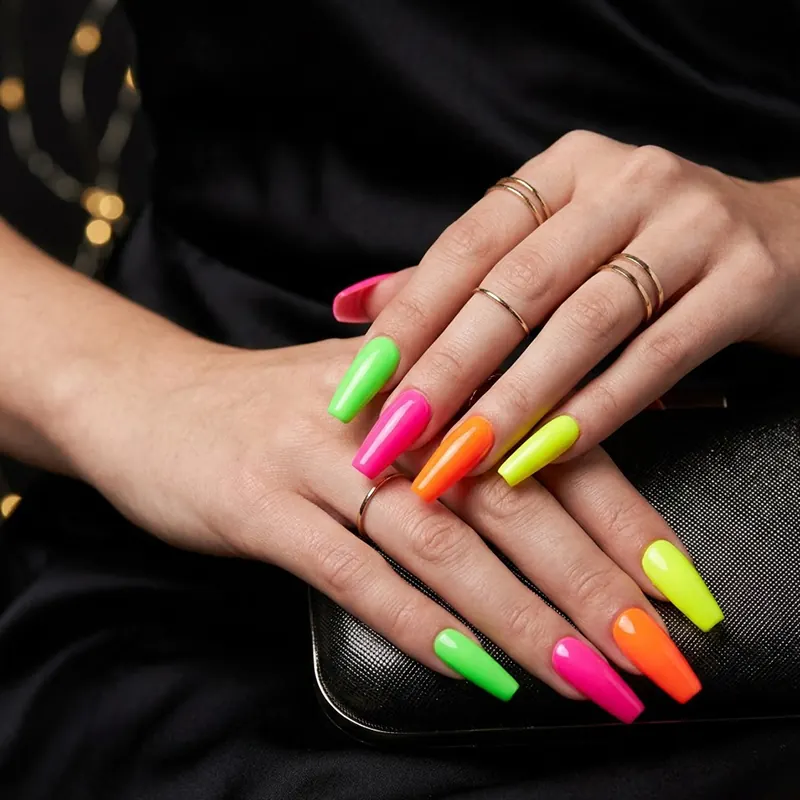 Prom Nails: Your Ultimate Guide to Stunning Styles and Techniques 2026 13 Professional close-up of long coffin-shaped prom nails in vibrant neon shades of electric pink, lime green, punchy orange, and bright yellow, accessorized with minimalist gold rings against a black dress.