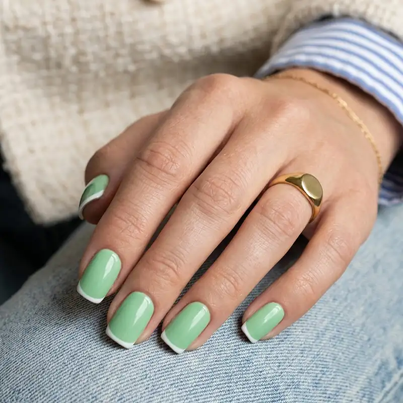 High-resolution close-up photo of medium squoval nails painted in a trendy pastel Kelly green with an ultra-thin white French tip, showcasing modern preppy summer nails.